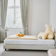 Ein gemütliches Bett in einem einladenden Raum, umgeben von warmen Farben und sanfter Beleuchtung.